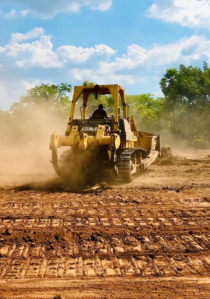 A yellow bulldozer working on a dusty construction site, moving earth under a clear sky.